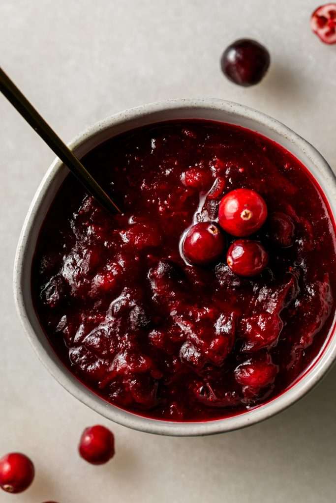 Bowl of homemade ruby red cranberry sauce with whole berries and agave gold spoon.