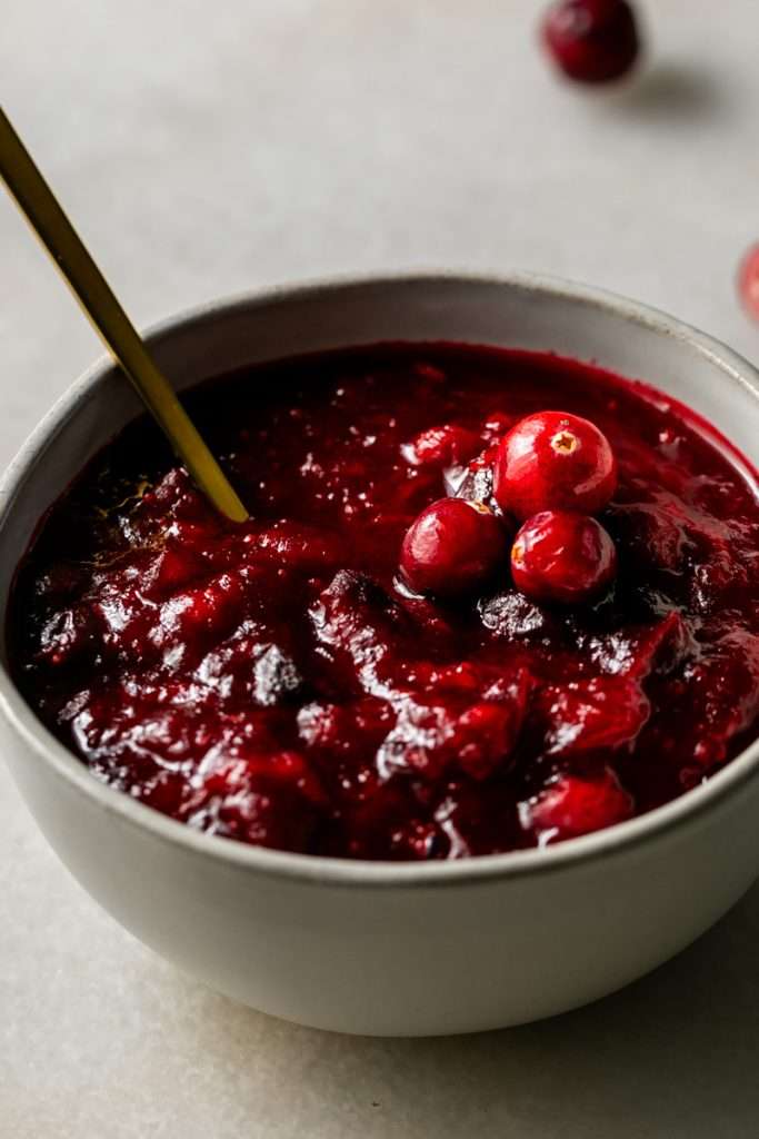 Bowl of homemade ruby red cranberry sauce with whole berries and agave gold spoon