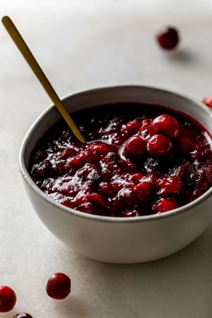 Bowl of homemade ruby red cranberry sauce with whole berries and agave gold spoon