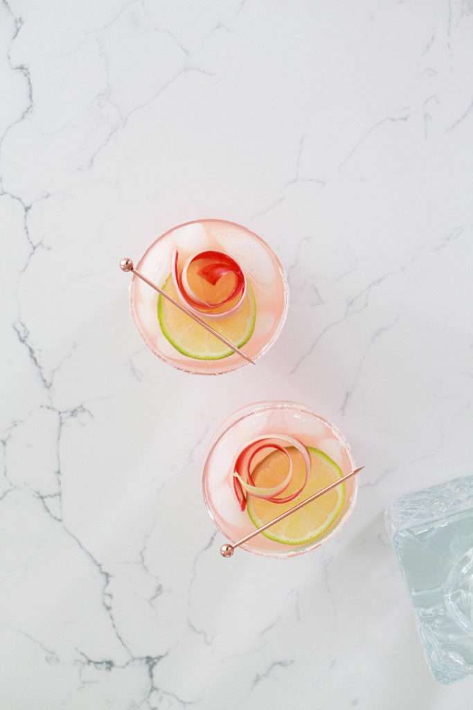 Refreshing rhubarb paloma cocktail with tequila, grapefruit, juice and lime, garnished with rhubarb ribbons and citrus slices.