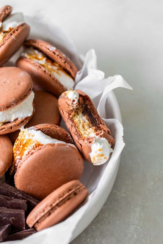Don't let summer come to an end without making a batch of these S'mores macarons. Complete with chocolate macaron shells, homemade marshamallows, graham crackers and dark chocolate, they are the ultimate s'mores dessert for the season! Dairy free and gluten free option included.