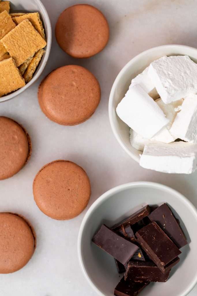 Don't let summer come to an end without making a batch of these S'mores macarons. Complete with chocolate macaron shells, homemade marshamallows, graham crackers and dark chocolate, they are the ultimate s'mores dessert for the season! Dairy free and gluten free option included.