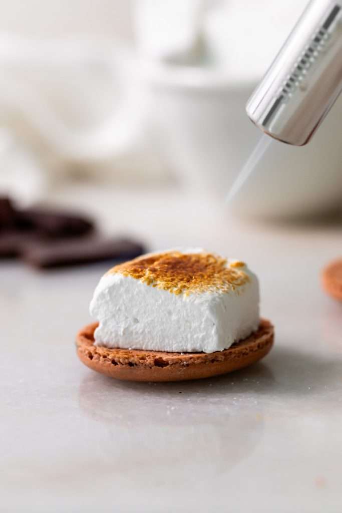 Don't let summer come to an end without making a batch of these S'mores macarons. Complete with chocolate macaron shells, homemade marshamallows, graham crackers and dark chocolate, they are the ultimate s'mores dessert for the season! Dairy free and gluten free option included.
