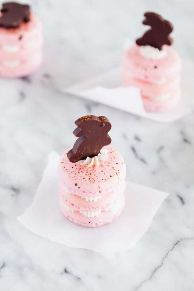Chocolate bunny macarons stacks, 3 shells high, layered with speckled macaron shells, vanilla frosting and finished with cute chocolate bunnies. Perfect for your Easter Sunday brunch dessert menus.