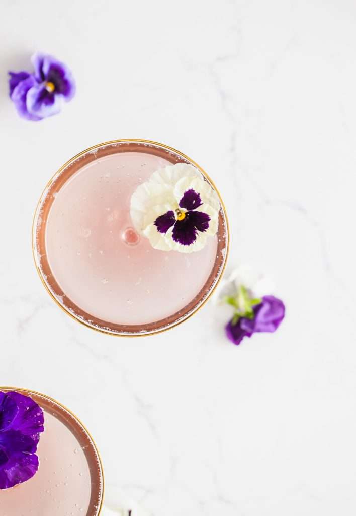 Floral spring champagne cocktail made with cream de Violette, lemon, and champagne, served in coupe glasses with flower garnish.