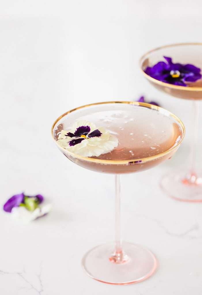 Floral spring champagne cocktail made with cream de Violette, lemon, and champagne, served in coupe glasses with flower garnish.
