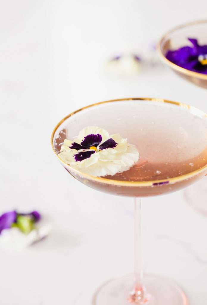 Floral spring champagne cocktail made with cream de Violette, lemon, and champagne, served in coupe glasses with flower garnish.