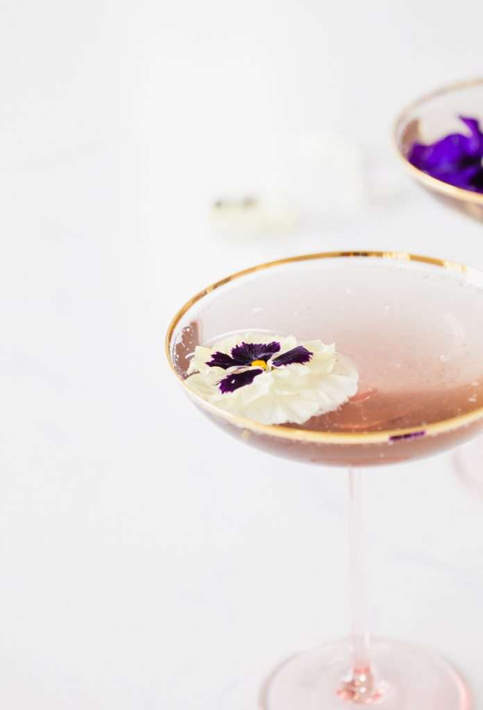Floral spring champagne cocktail made with cream de Violette, lemon, and champagne, served in coupe glasses with flower garnish.