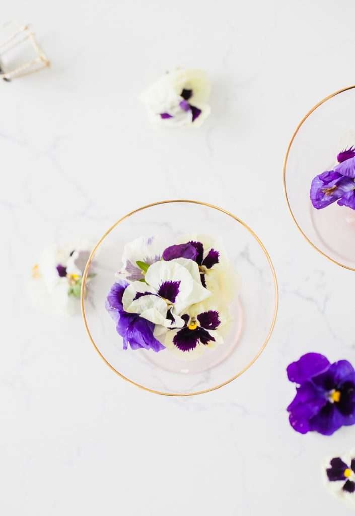 Floral spring champagne cocktail made with cream de Violette, lemon, and champagne, served in coupe glasses with flower garnish.