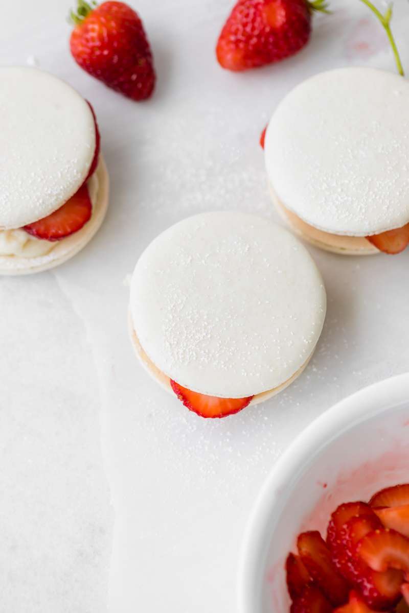 Strawberry shortcake macarons recipe, made with French macaron shells, fresh strawberries and vanilla whip frosting. Dairy and gluten free