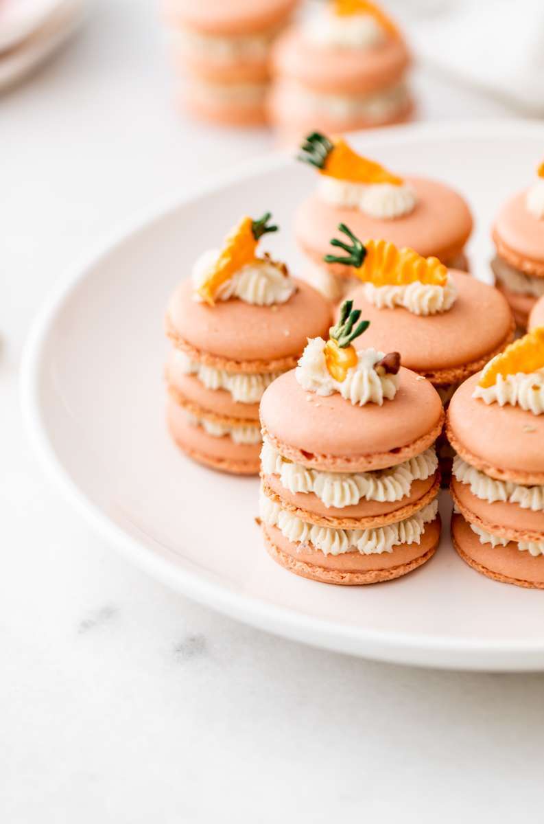 Carrot cake macaron stacks made with cinnamon frosting and carrot cake filling. Decorated with carrot icing decorations. Dairy & Gluten Free and perfect for Easter dessert menus!