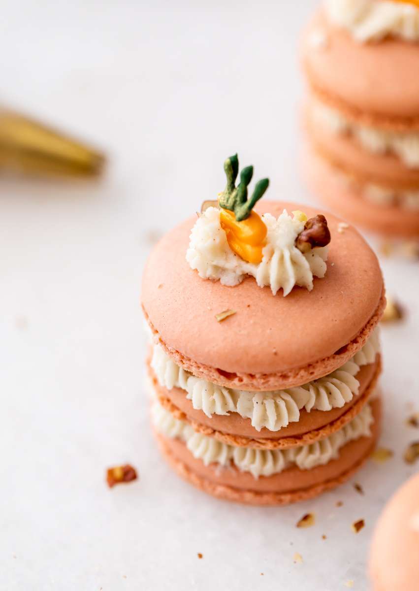 Carrot cake macaron stacks made with cinnamon frosting and carrot cake filling. Decorated with carrot icing decorations. Dairy & Gluten Free and perfect for Easter dessert menus!