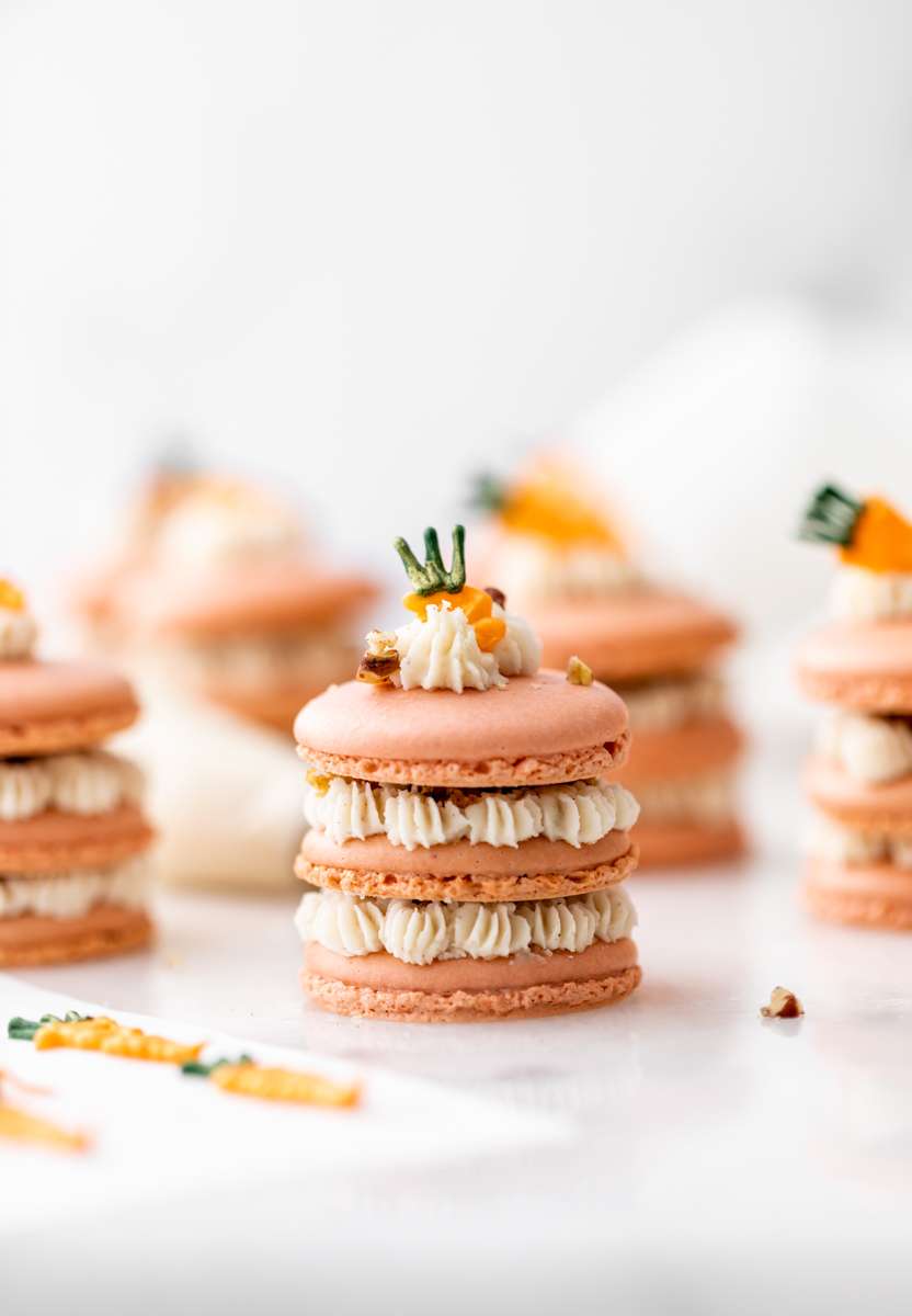 Carrot cake macaron stacks made with cinnamon frosting and carrot cake filling. Decorated with carrot icing decorations. Dairy & Gluten Free and perfect for Easter dessert menus!