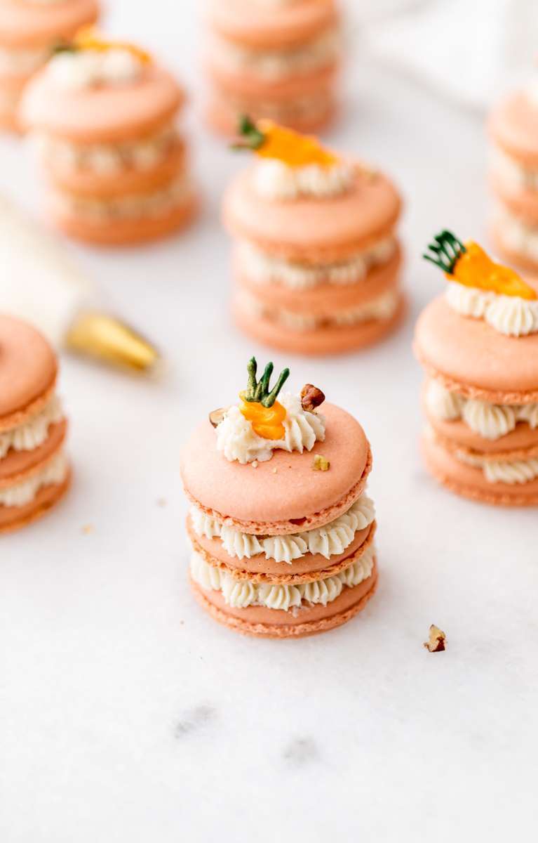 Carrot cake macaron stacks made with cinnamon frosting and carrot cake filling. Decorated with carrot icing decorations. Dairy & Gluten Free and perfect for Easter dessert menus!