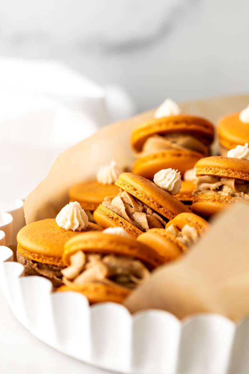 Pumpkin pie flavored French macarons, complete with pumpkin pie frosting, pie crust center, and a dollop vanilla frosting on top! The perfect one bite dessert for Thanksgiving menus. Dairy free