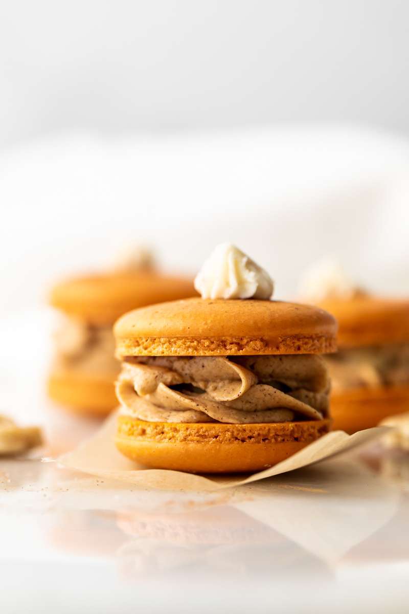 Pumpkin pie flavored French macarons, complete with pumpkin pie frosting, pie crust center, and a dollop vanilla frosting on top! The perfect one bite dessert for Thanksgiving menus. Dairy free