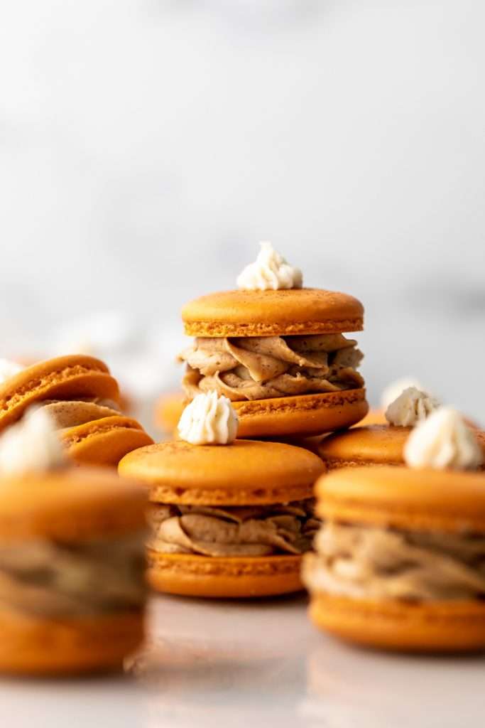 Pumpkin pie flavored French macarons, complete with pumpkin pie frosting, pie crust center, and a dollop vanilla frosting on top! The perfect one bite dessert for Thanksgiving menus. Dairy free