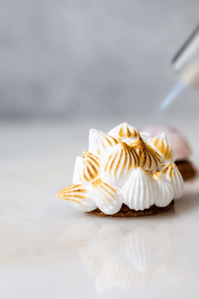 Baked Alaska Macarons, with a chocolate macaron shell base, raspberry ice cream core, topped with torched Italian meringue. A modern bite-sized spin on the classic Baked Alaska dessert. Dairy Free & Gluten Free