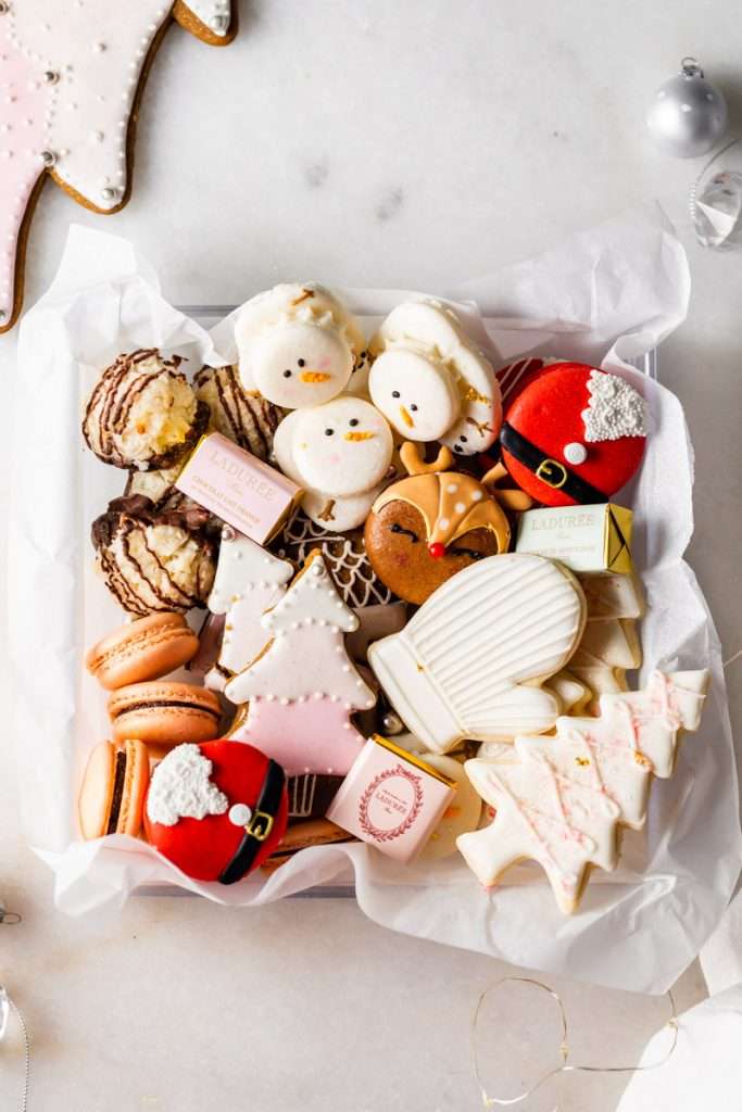 An elegant box of Christmas cookies with macarons, sugar cookies and more in shades of pink.