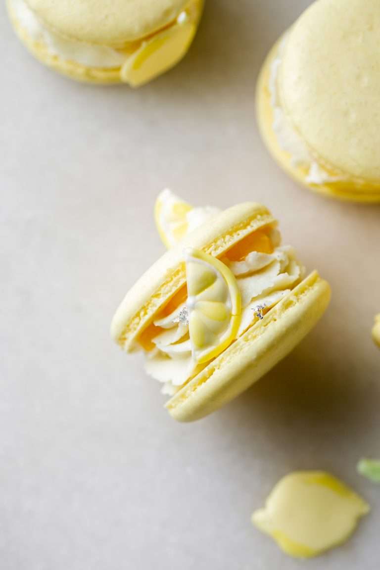 Lemon flavored French macarons filled with lemon vanilla bean frosting and lemon curd. Decorated with royal icing transfers. A dairy free and gluten free macaron recipe perfect for spring and summer.