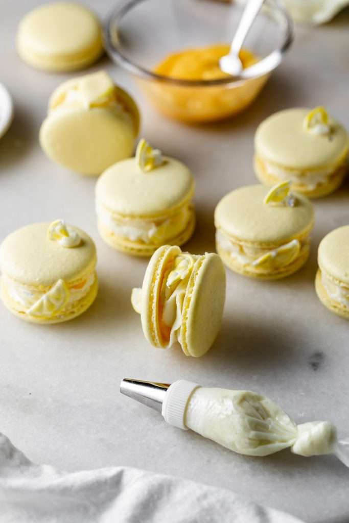 Lemon flavored French macarons filled with lemon vanilla bean frosting and lemon curd. Decorated with royal icing transfers. A dairy free and gluten free macaron recipe perfect for spring and summer.