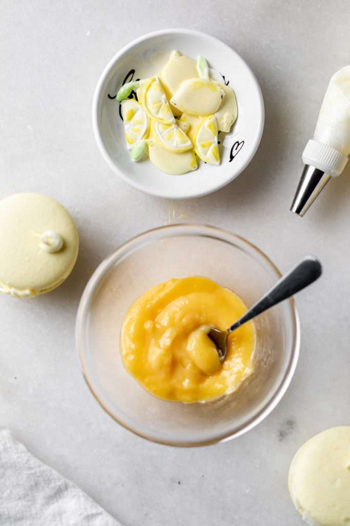 Lemon flavored French macarons filled with lemon vanilla bean frosting and lemon curd. Decorated with royal icing transfers. A dairy free and gluten free macaron recipe perfect for spring and summer.
