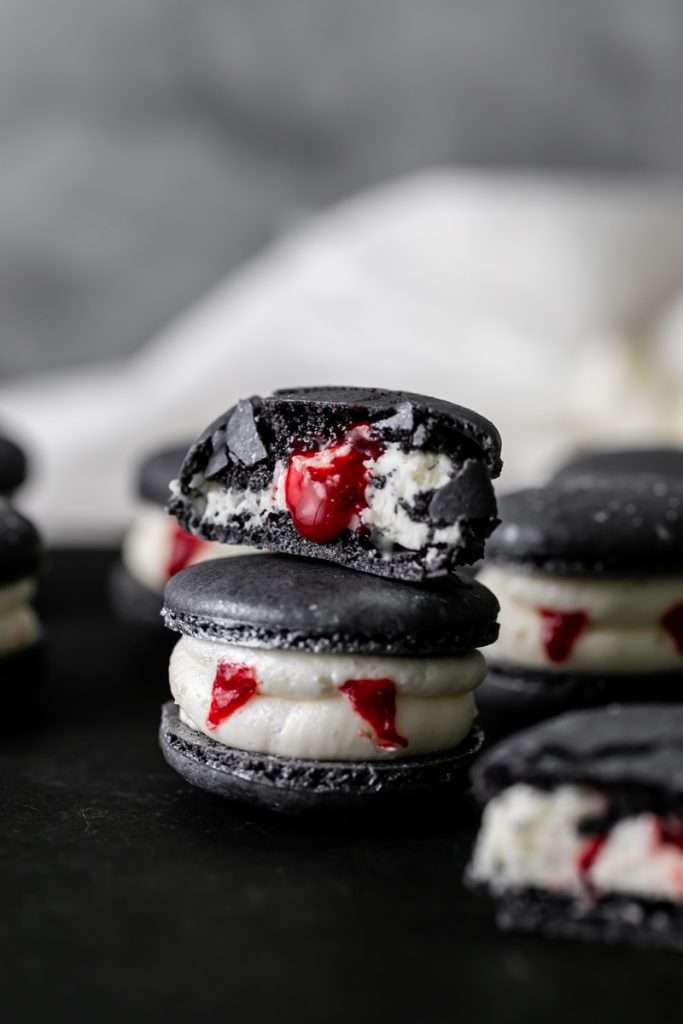 Easy Vampire decorated macarons for Halloween, with black cocoa shells, vanilla bean frosting and strawberry jam. A spooky sweet macaron for the fall season! Dairy free & Gluten free