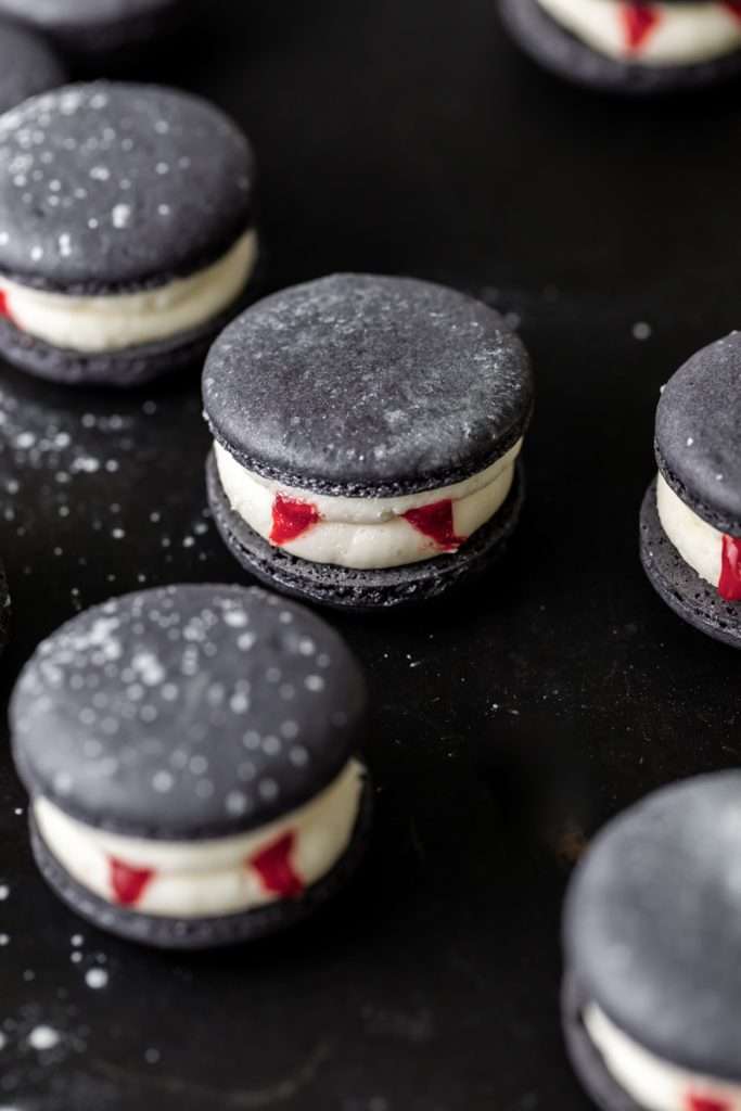 Easy Vampire decorated macarons for Halloween, with black cocoa shells, vanilla bean frosting and strawberry jam. A spooky sweet macaron for the fall season! Dairy free & Gluten free