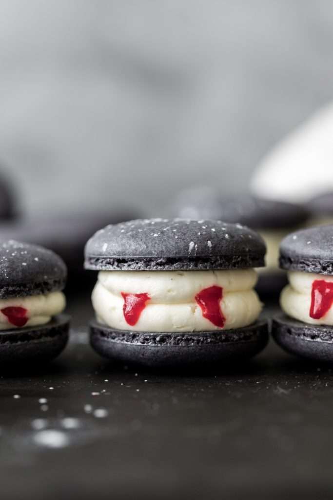 Easy Vampire decorated macarons for Halloween, with black cocoa shells, vanilla bean frosting and strawberry jam. A spooky sweet macaron for the fall season! Dairy free & Gluten free