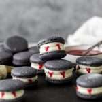 Easy Vampire decorated macarons for Halloween, with black cocoa shells, vanilla bean frosting and strawberry jam. A spooky sweet macaron for the fall season! Dairy free & Gluten free