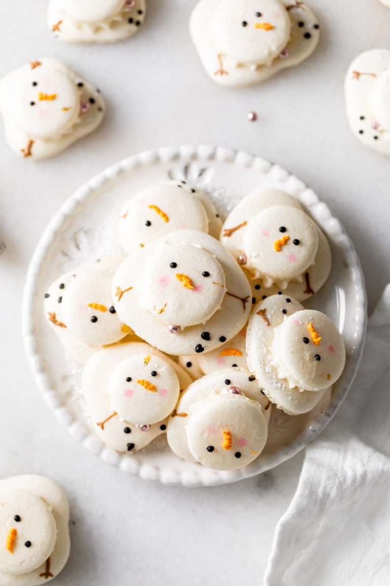Cute melted snowman French macarons filled with vanilla frosting and finished with easy royal icing decorations, inspired by the popular melted snowman cookies! They're dairy free, gluten free and a fun treat to add to your holiday baking plans this season!