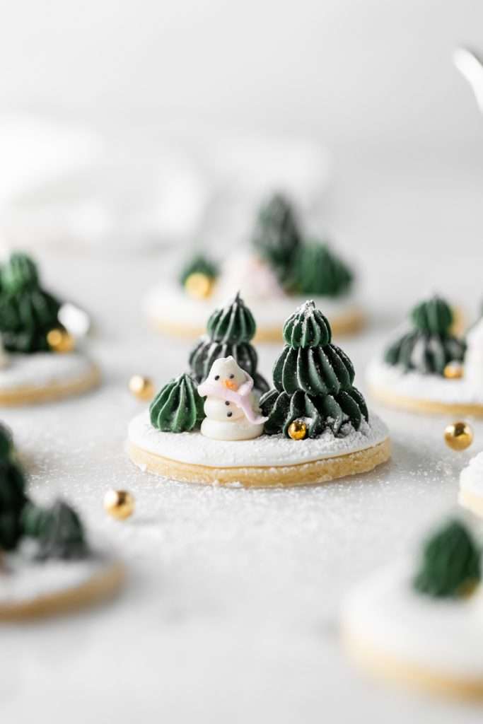 Winter themed roll out sugar cookies, flooded with a royal icing base and decorated with easy three dimension trees and snowmen, using star and round piping tips. The Christmas cookie design requires little decorating experience and will be perfect for your next holiday party or cookie exchange! 