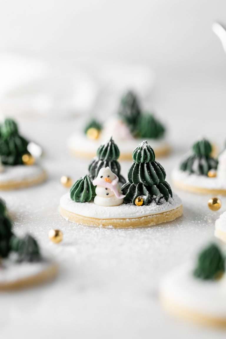 Cute winter themed sugar cookies, simply flooded with a royal icing base, then decorated with easy three dimension trees and snowmen, using star and round piping tips. This simple Christmas cookie design requires little experience with royal icing to complete from start to finish!