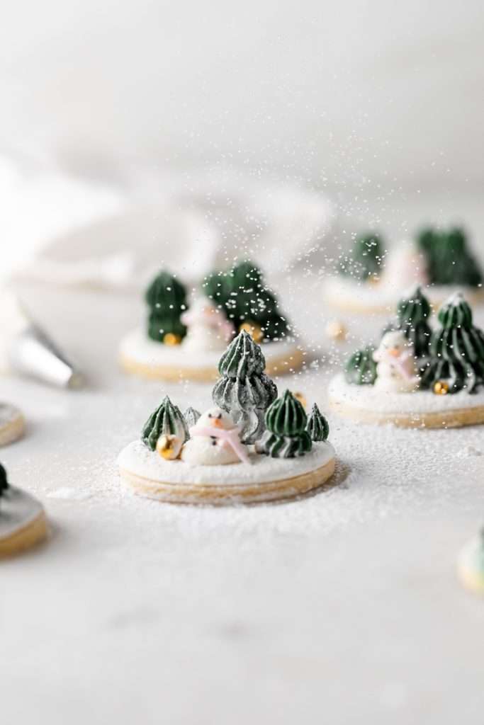 Winter themed roll out sugar cookies, flooded with a royal icing base and decorated with easy three dimension trees and snowmen, using star and round piping tips. The Christmas cookie design requires little decorating experience and will be perfect for your next holiday party or cookie exchange! 