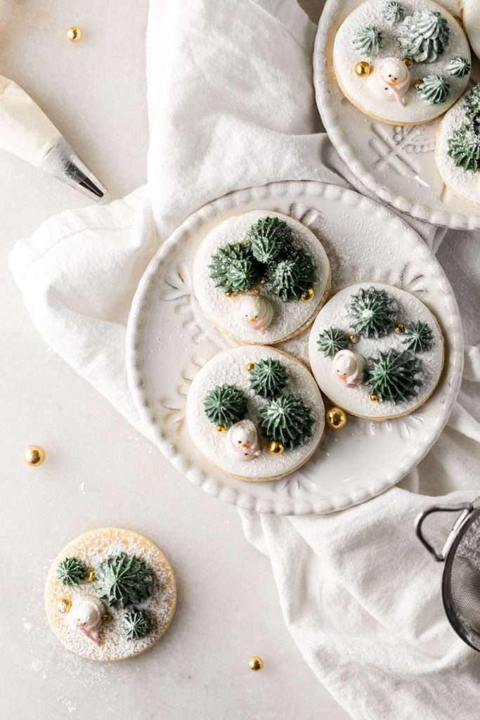 Winter themed roll out sugar cookies, flooded with a royal icing base and decorated with easy three dimension trees and snowmen, using star and round piping tips. The Christmas cookie design requires little decorating experience and will be perfect for your next holiday party or cookie exchange! 
