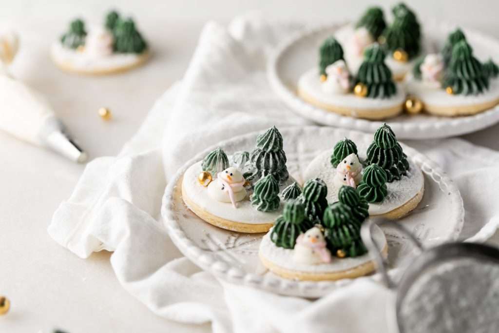 Winter themed roll out sugar cookies, flooded with a royal icing base and decorated with easy three dimension trees and snowmen, using star and round piping tips. The Christmas cookie design requires little decorating experience and will be perfect for your next holiday party or cookie exchange! 