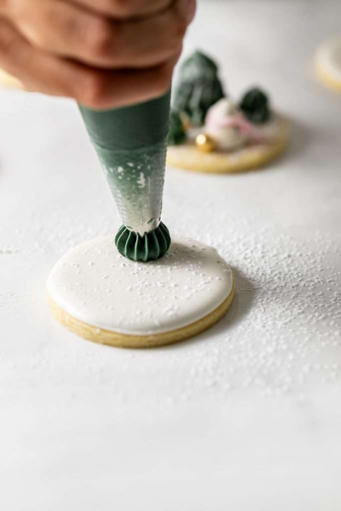 Winter themed roll out sugar cookies, flooded with a royal icing base and decorated with easy three dimension trees and snowmen, using star and round piping tips. The Christmas cookie design requires little decorating experience and will be perfect for your next holiday party or cookie exchange! 