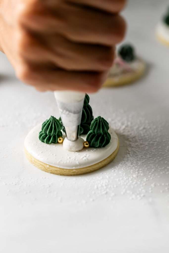 Winter themed roll out sugar cookies, flooded with a royal icing base and decorated with easy three dimension trees and snowmen, using star and round piping tips. The Christmas cookie design requires little decorating experience and will be perfect for your next holiday party or cookie exchange! 