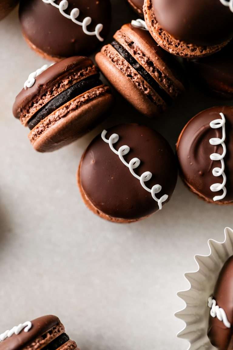 Hostess cupcake macarons recipe, a play on the original, filled with rich dark chocolate frosting and fluffy marshmallow filling. The shells are dipped in dark chocolate and decorated with icing loops to complete the look and taste! Check out the recipe, video and step by step instructions. Dairy free and gluten free option.