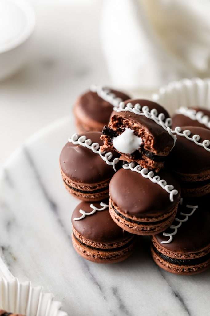 Hostess cupcake inspired macarons, with rich dark chocolate frosting and fluffy marshmallow filling. The shells are dipped in dark chocolate and decorated with icing loops to complete the look and taste! Check out the recipe, video and step by step instructions. Dairy free and gluten free option.