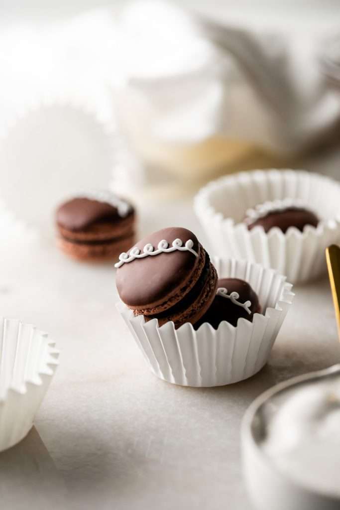 Hostess cupcake inspired macarons, with rich dark chocolate frosting and fluffy marshmallow filling. The shells are dipped in dark chocolate and decorated with icing loops to complete the look and taste! Check out the recipe, video and step by step instructions. Dairy free and gluten free option.