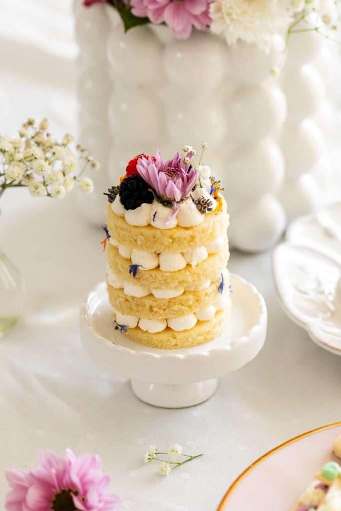 Mini birthday cake topped with fresh berries, flowers and vanilla frosting. Perfect for summer parties.