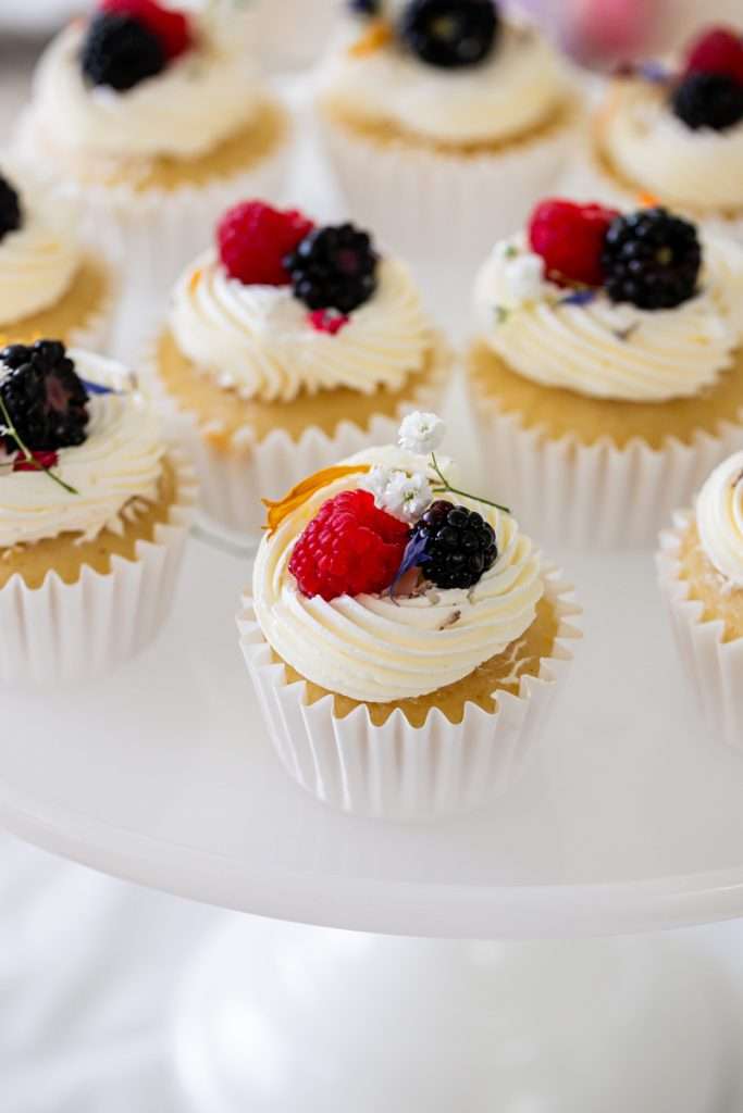 Vanilla cupcakes with fresh berries and flower garnish for - Flower themed teen Birthday party.
