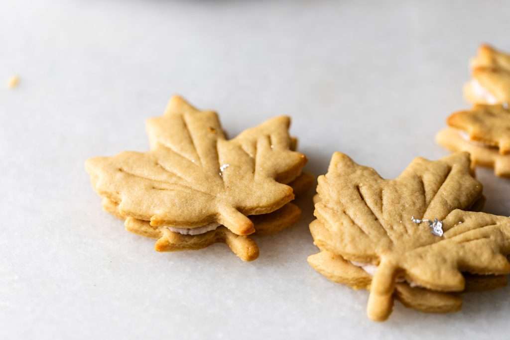 Easy and delicious maple leaf cookies, inspired by Canadian maple cookies filled with maple buttercream and simply decorated with edible gold. A wonderful treat for the fall season and for upcoming fall gatherings. Dairy free option included.