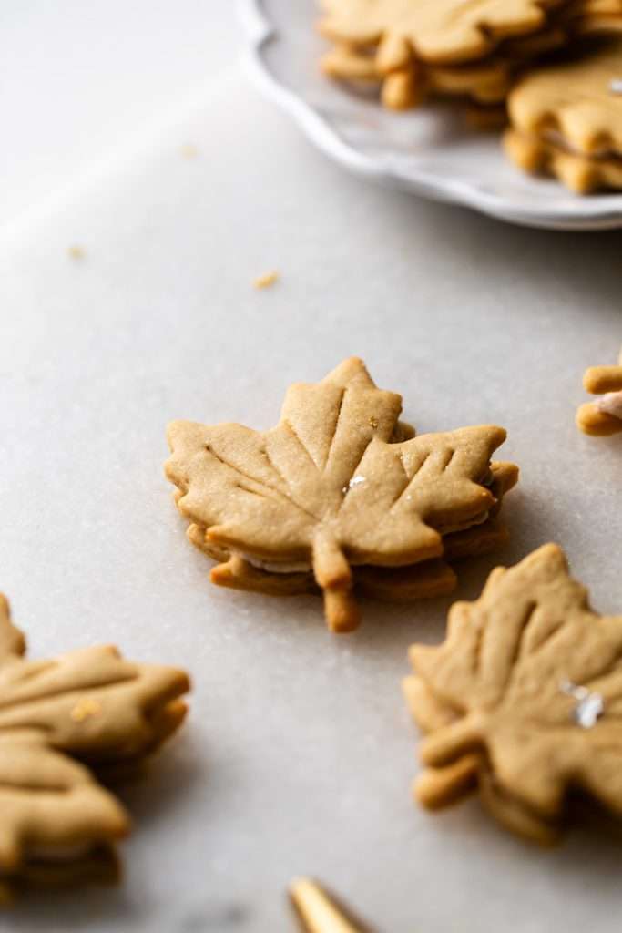 Easy and delicious maple leaf cookies, inspired by Canadian maple cookies filled with maple buttercream and simply decorated with edible gold. A wonderful treat for the fall season and for upcoming fall gatherings. Dairy free option included.
