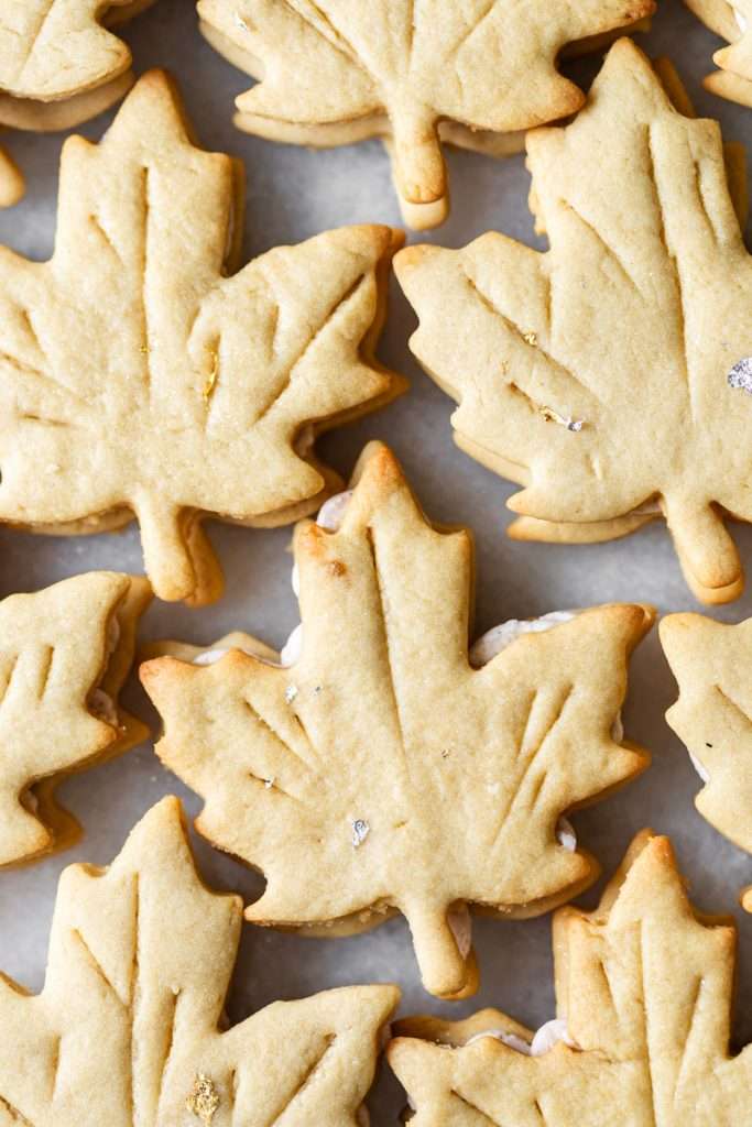 Easy and delicious maple leaf cookies, inspired by Canadian maple cookies filled with maple buttercream and simply decorated with edible gold. A wonderful treat for the fall season and for upcoming fall gatherings. Dairy free option included.