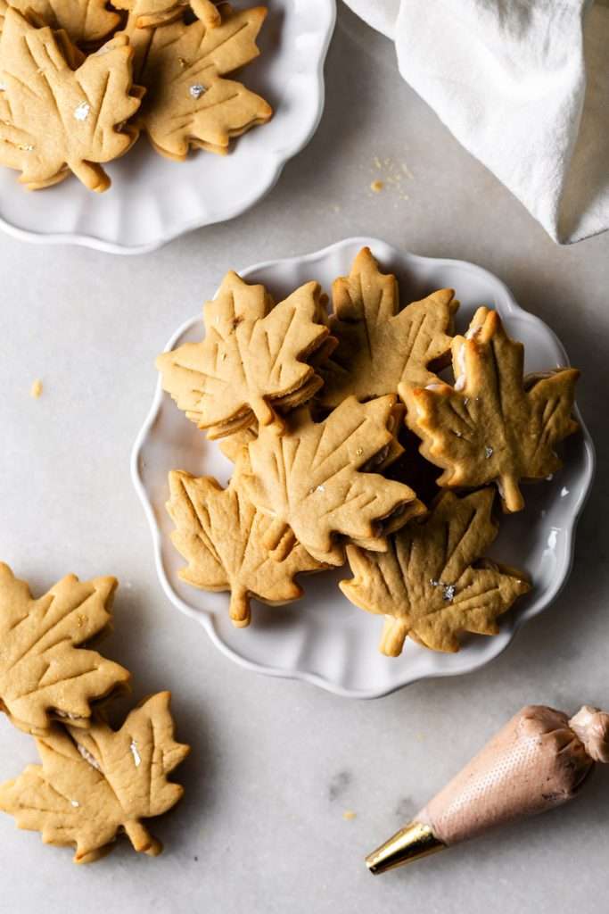 Easy and delicious maple leaf cookies, inspired by Canadian maple cookies filled with maple buttercream and simply decorated with edible gold. A wonderful treat for the fall season and for upcoming fall gatherings. Dairy free option included.