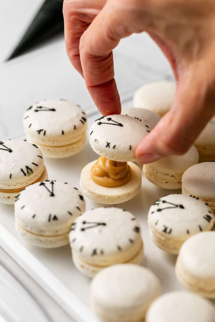 New Years Eve Macarons with royal icing clock decorations for a macaron cube cake. Filled with biscoff ganache.