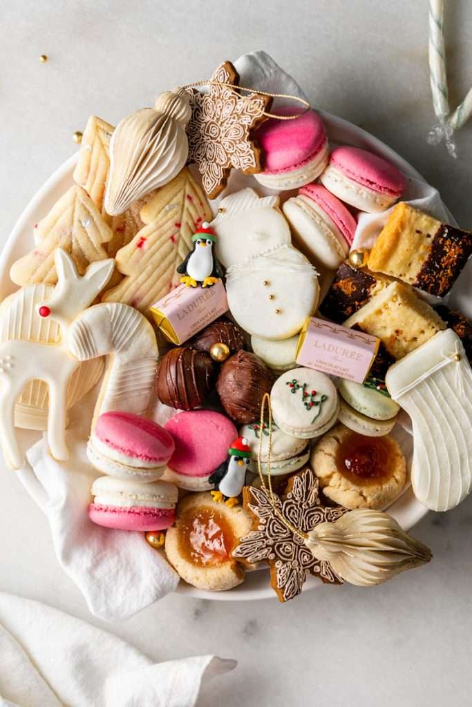 A platter of Christmas cookies and treats, complete with macarons, sugar cookies, jam thumbprints gingerbread, chocolates and more.