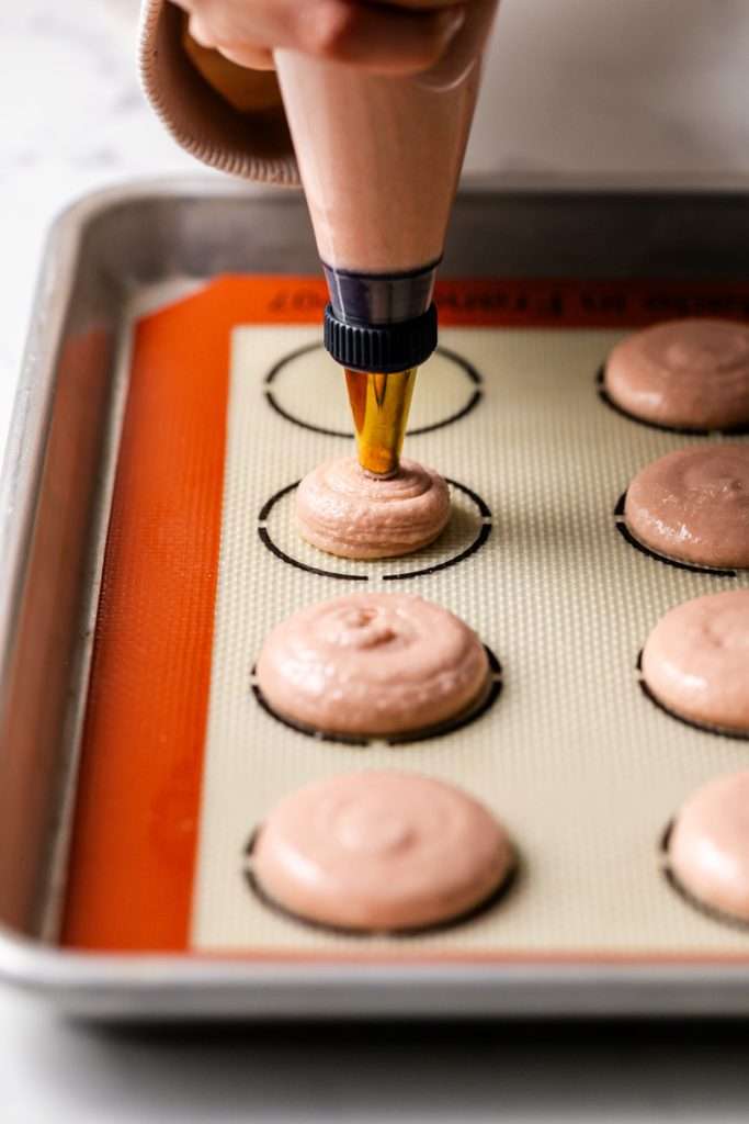 Piping Italian macaron shells with a size 12 round piping tip on a silpat mat.